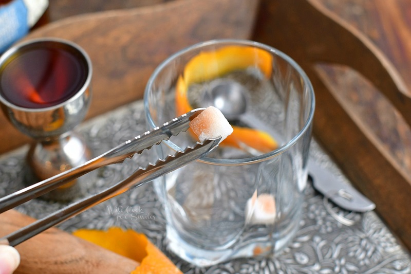 holding sugar cube in metal tongs over a cocktail glass