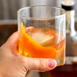 woman's hand holding cocktail over ice in low ball glass with orange peel