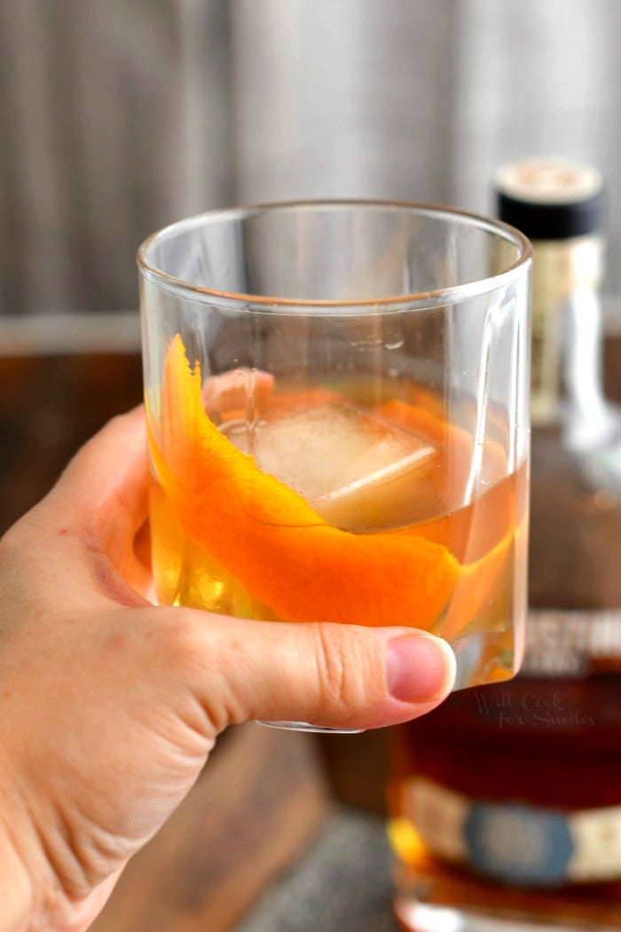 woman's hand holding cocktail over ice in low ball glass with orange peel