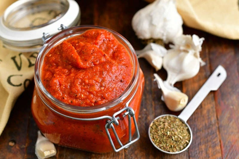 pizza sauce without tomato paste in small glass jar next to fresh garlic cloves and dried oregano