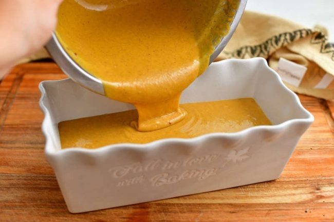 pouring batter into white ceramic loaf pan to make a moist pumpkin bread recipe