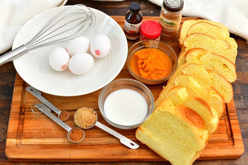 sliced bread, eggs, pumpkin, milk, and spices laid out on the cutting board