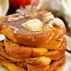 stack of Pumpkin French toast on a plate topped with scoop of butter, syrup, and powdered sugar