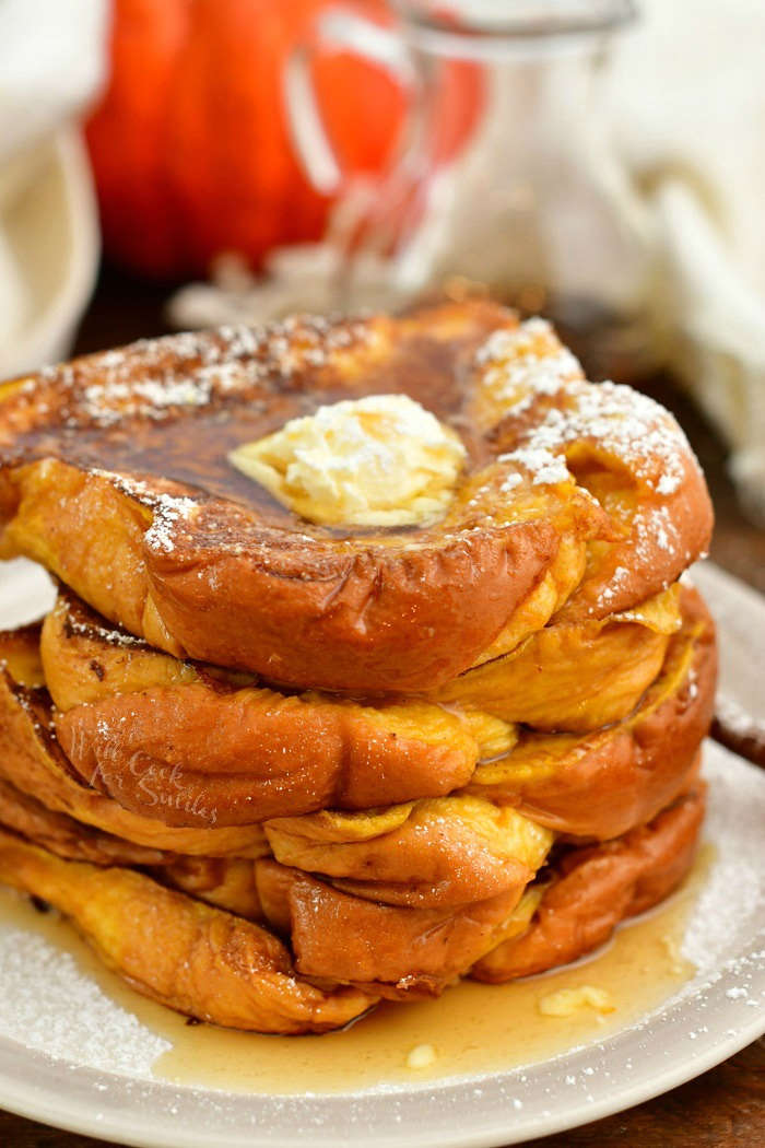 stack of Pumpkin French toast on a plate topped with scoop of butter, syrup, and powdered sugar