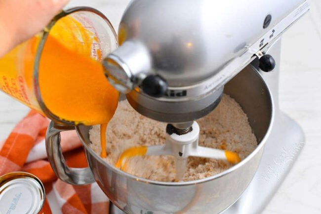 adding pumpkin puree mixture to bowl of a stand mixer with flour in it