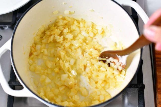 photo shows how to make tomato soup by sauteeing onions in large white pot on stove top