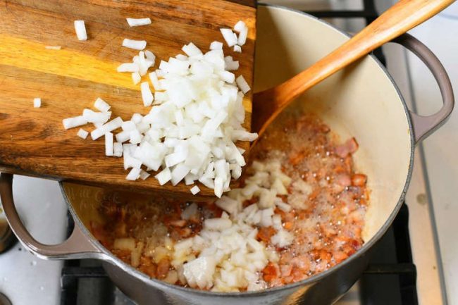 diced onion on wood cutting board being transferred to cooking pot