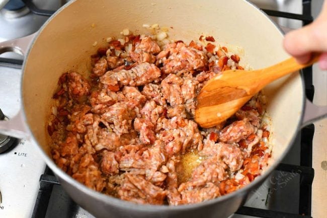 using wooden spoon to break up ground Italian sausage in Dutch oven