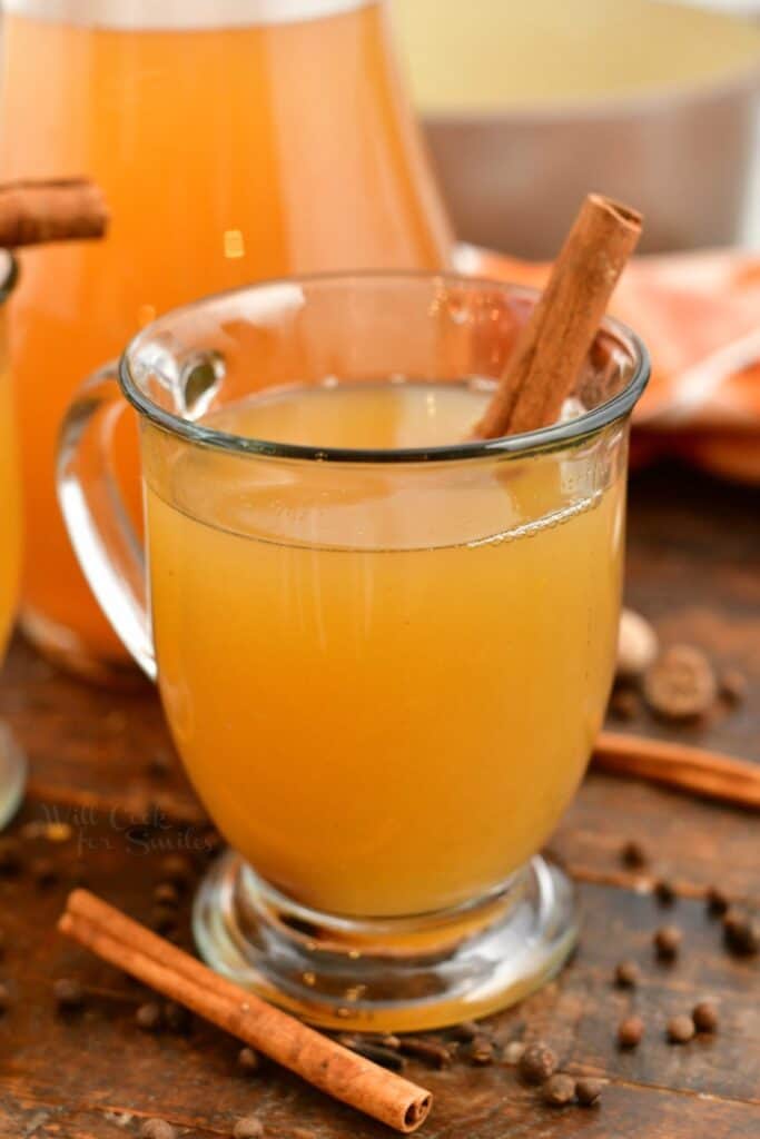 hot apple cider in glass mug garnished with cinnamon stick