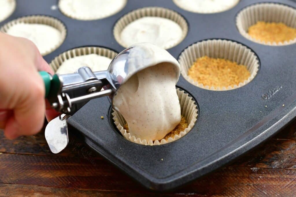 scooping cheesecake batter into cupcake liner in baking pan