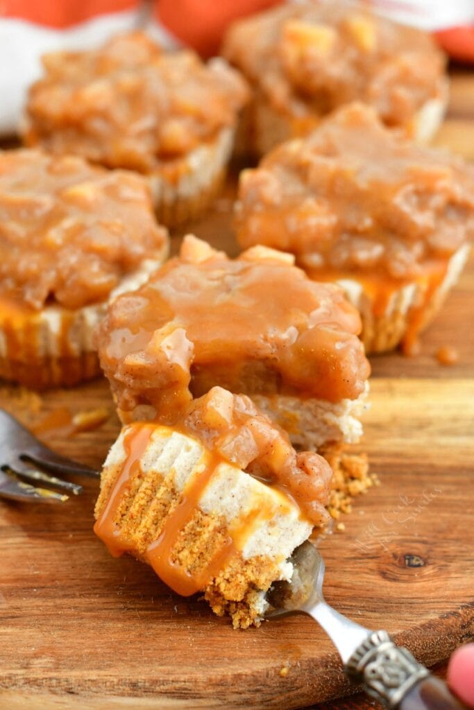 bite of apple mini cheesecake on a fork with individual cheesecakes behind it