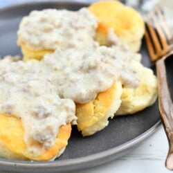 several biscuits covered in sausage gravy on a plate with w bronze fork