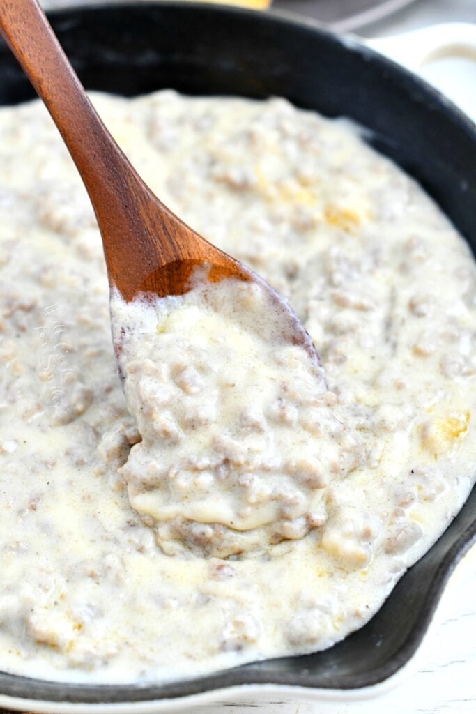 stirring white sausage gravy with a wooden spoon in a skillet