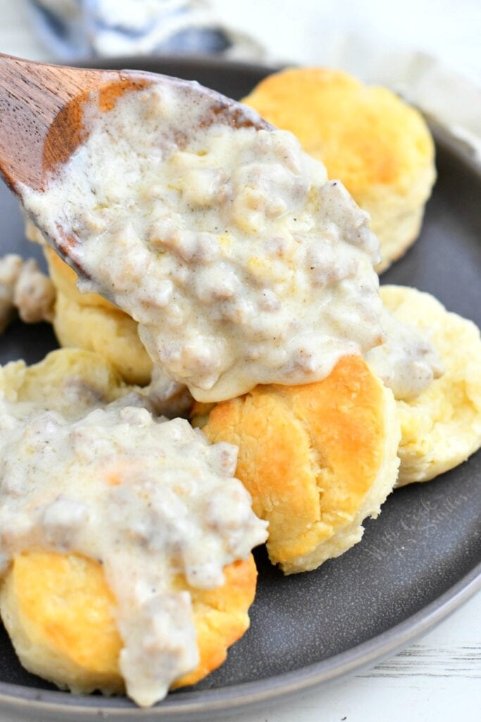 pouring white sausage gravy over biscuits using a wooden spoon