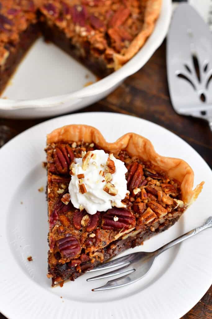plated slice of Thanksgiving chocolate pecan pie with rest of pie in background
