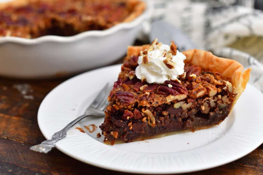 close up side view of chocolate pecan pie slice topped with whipped cream on on white plate