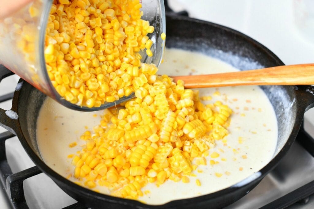 adding fresh corn niblets to a cast iron skillet with white sauce in it