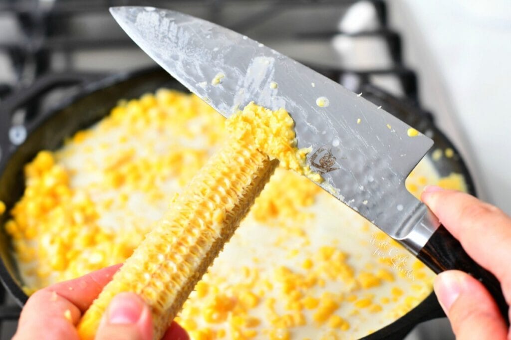 using the back of a chef's knife to remove fresh corn from a cob