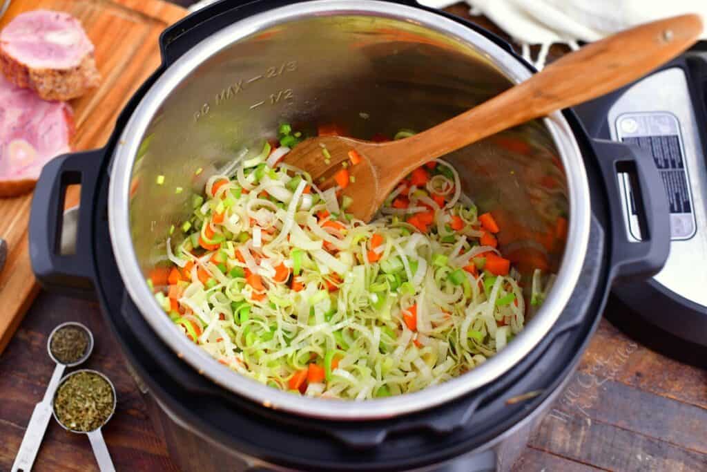 overhead image: stirring uncooked leeks and carrots in a pressure cooker