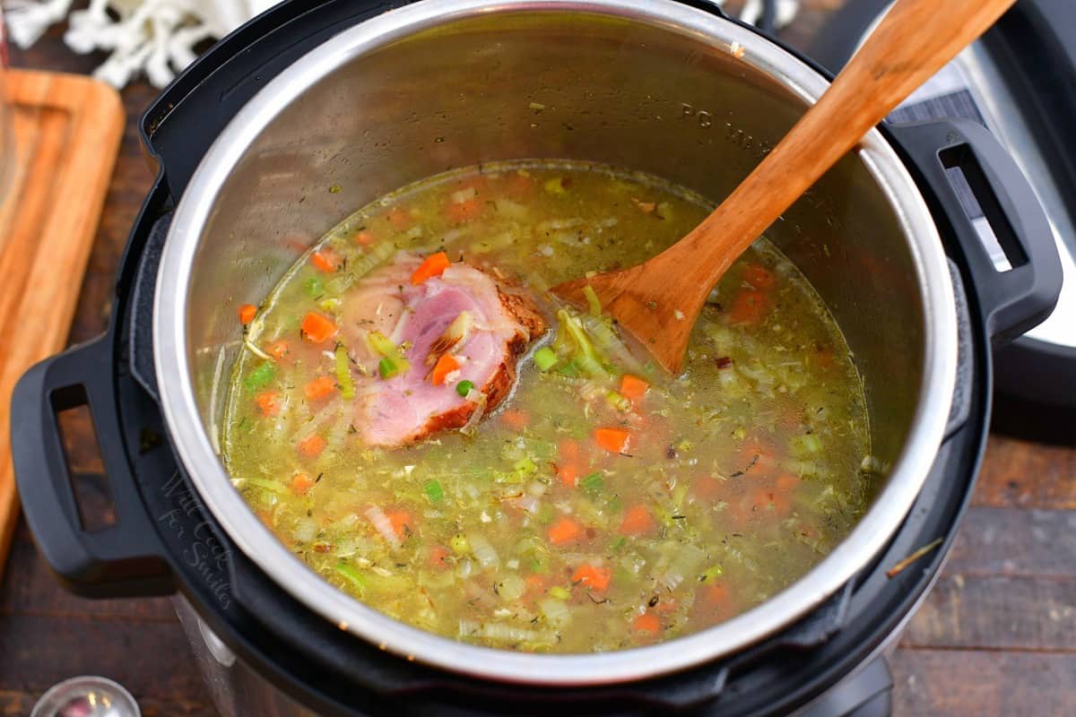 ham and vegetable soup in pressure cooker with wooden spoon.