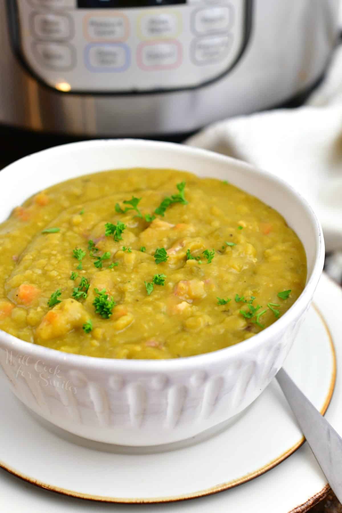 thick hearty split pea soup in white bowl with spoon on a plate.