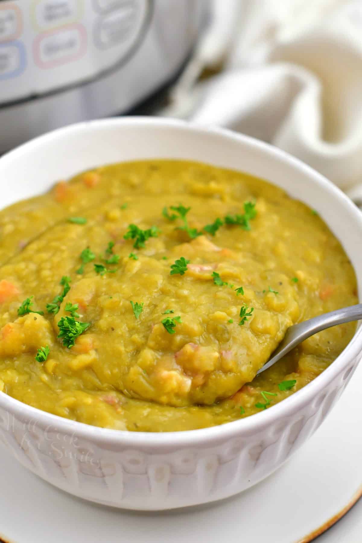 spooning some thick green split pea soup out of a white bowl.