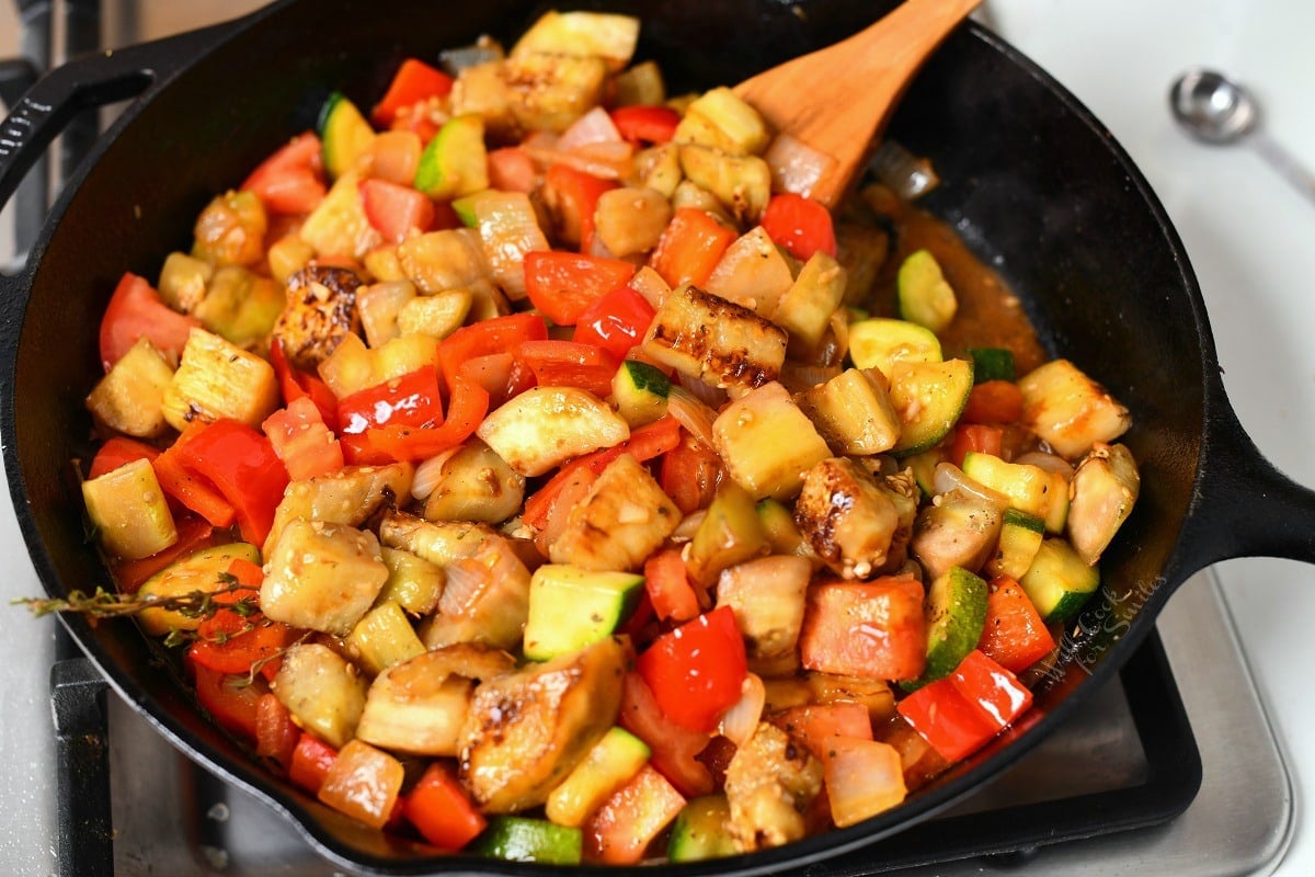 close up image of diced onions, red bell pepper, eggplant and zucchini cooking in cast iron skillet