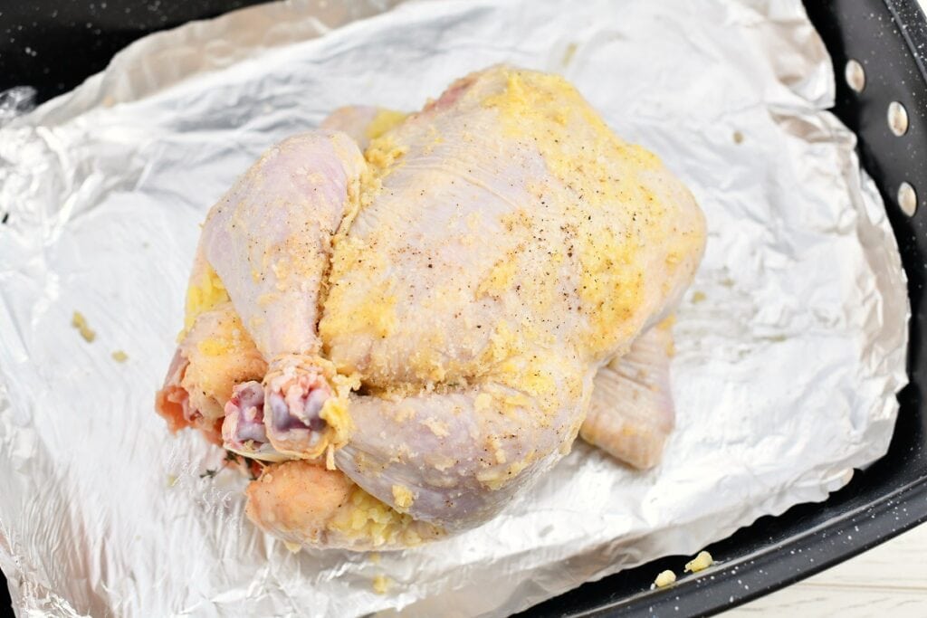 raw whole chicken with butter rubbed onto the skin in foil lined roasting pan