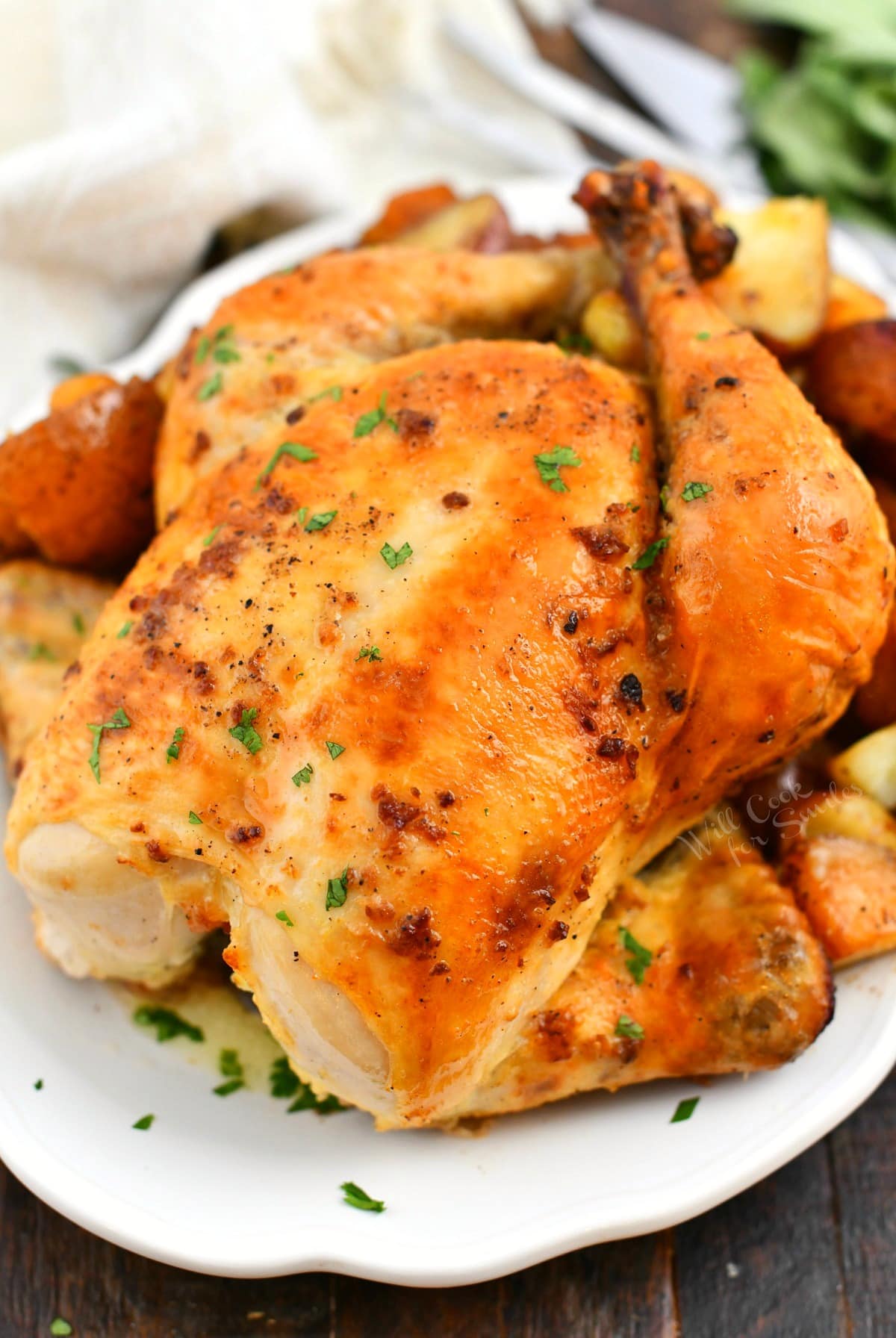 whole roasted chicken on white platter with potatoes around and parsley on top.