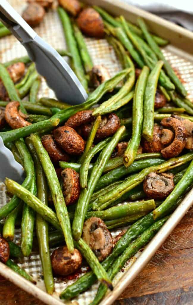 using tongs to toss roasted vegetables on a sheet pan