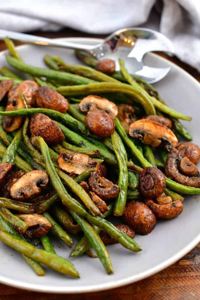 green bean and mushroom side dish in white bowl with serving spoon