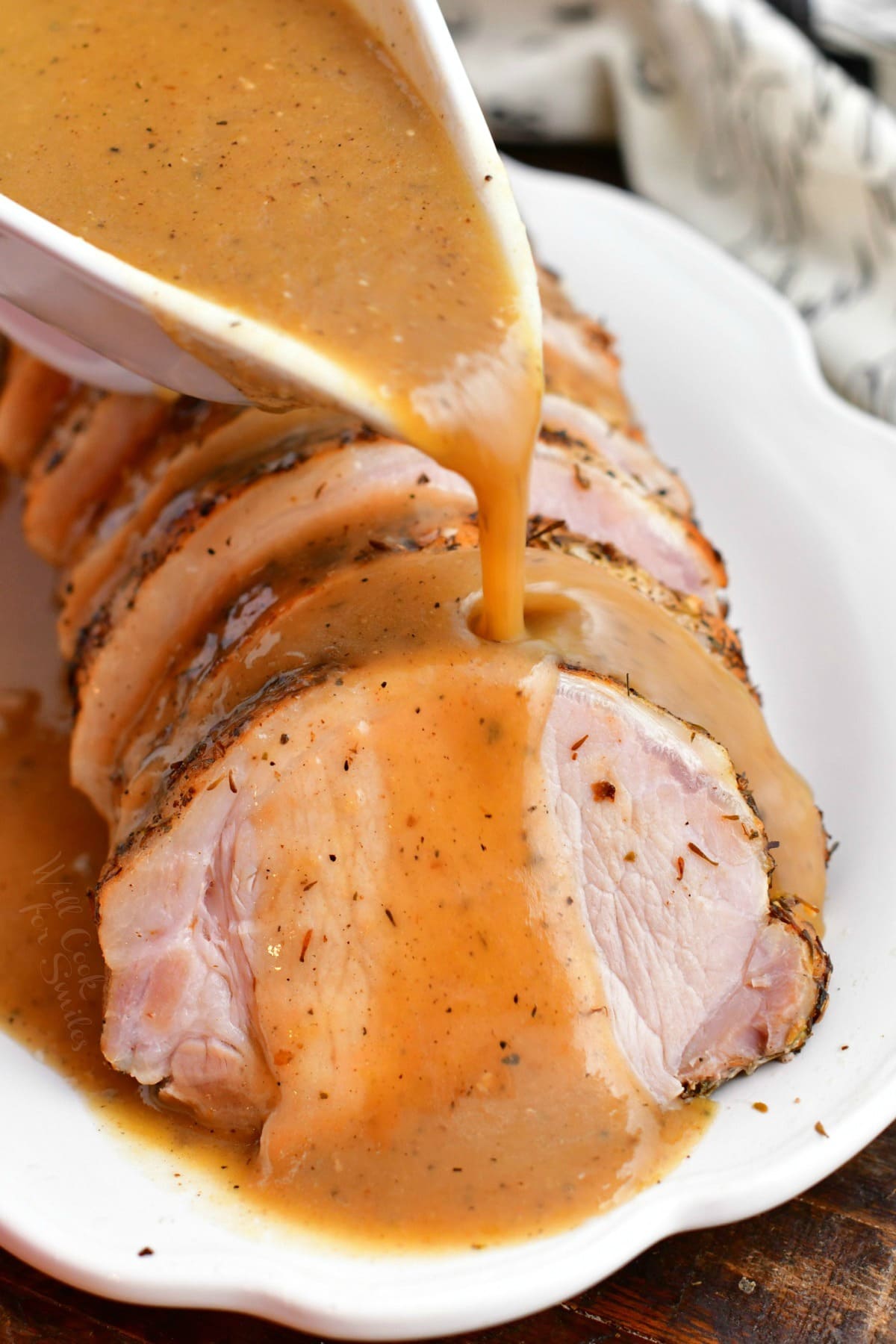 pouring brown gravy onto platter of pork roast slices