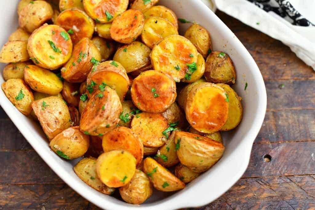 white dish of oven roasted potatoes with parsley and melted butter in white serving dish