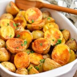 wooden spoon in white casserole dish with roasted potatoes