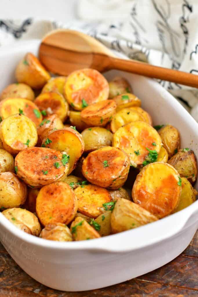 wooden spoon in white casserole dish with roasted potatoes