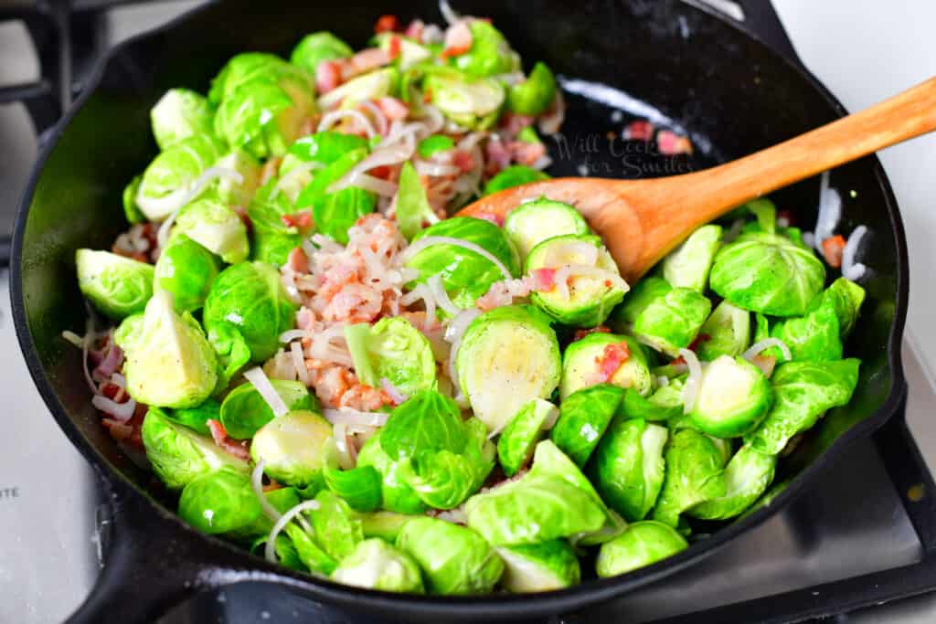 cooking green vegetables, shallot, and bacon in black skillet