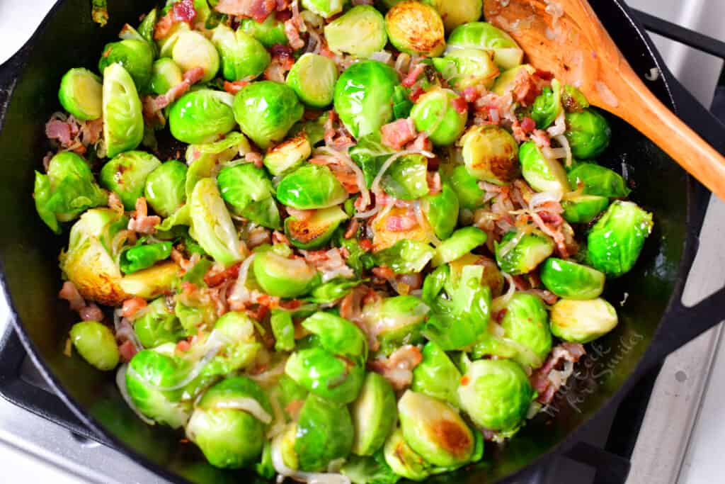 pan fried Brussels sprouts and bacon in skillet with wooden spoon
