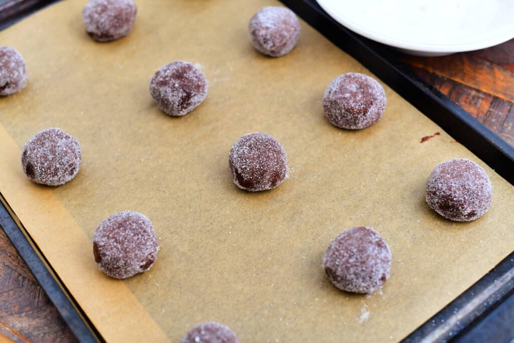 balls of chocolate cookie dough rolled in sugar on baking sheet