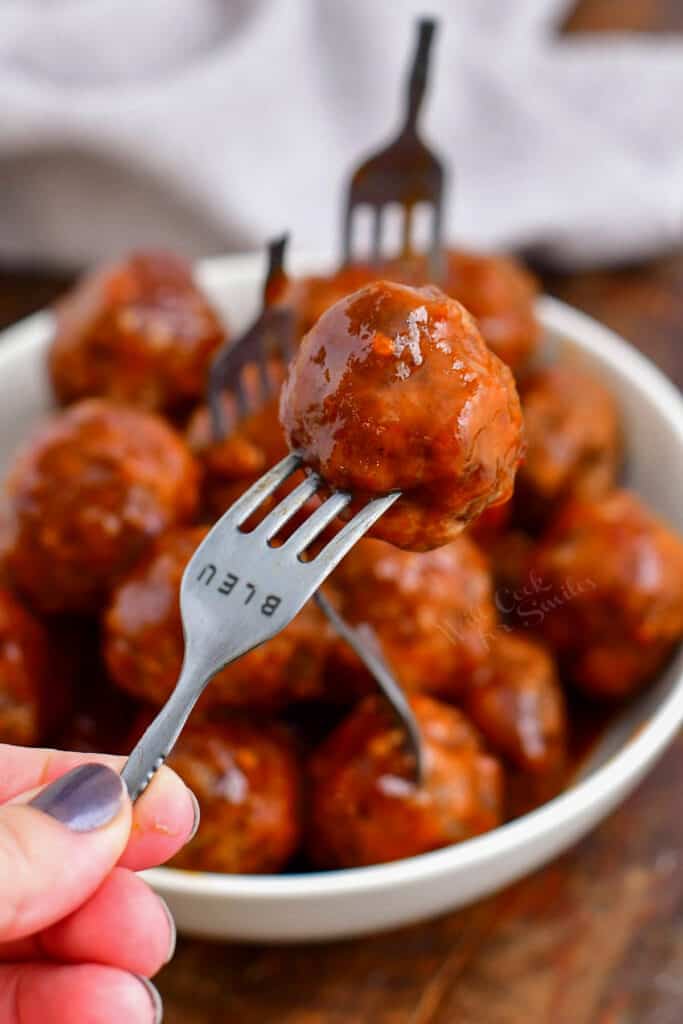 closeup image of cocktail meatball on a fork with bowl of meatballs in background
