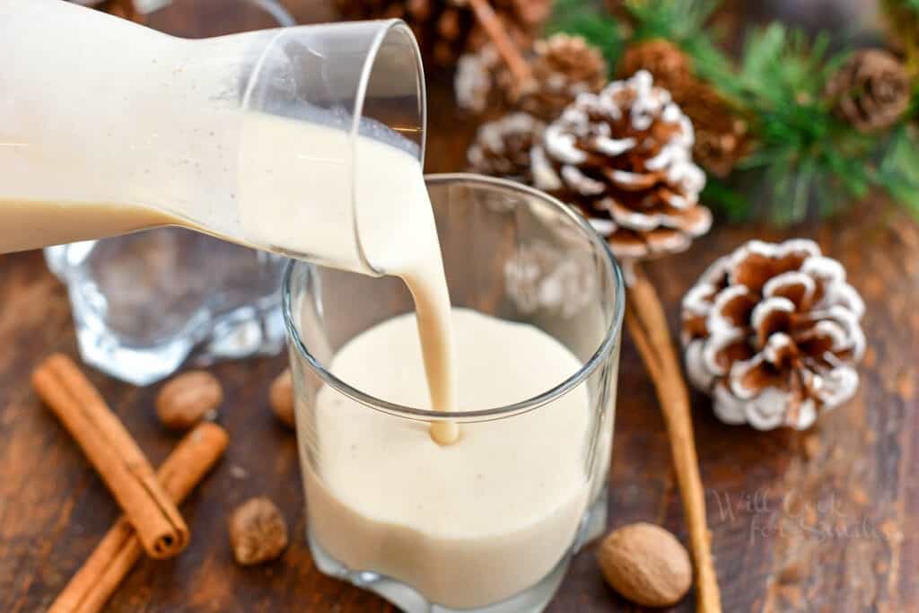 pouring coquito from glass pitcher into an Old Fashioned glass