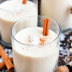 2 glasses of coquito garnished with cinnamon sticks and coconut flakes