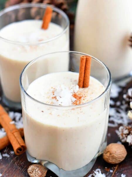 2 glasses of coquito garnished with cinnamon sticks and coconut flakes