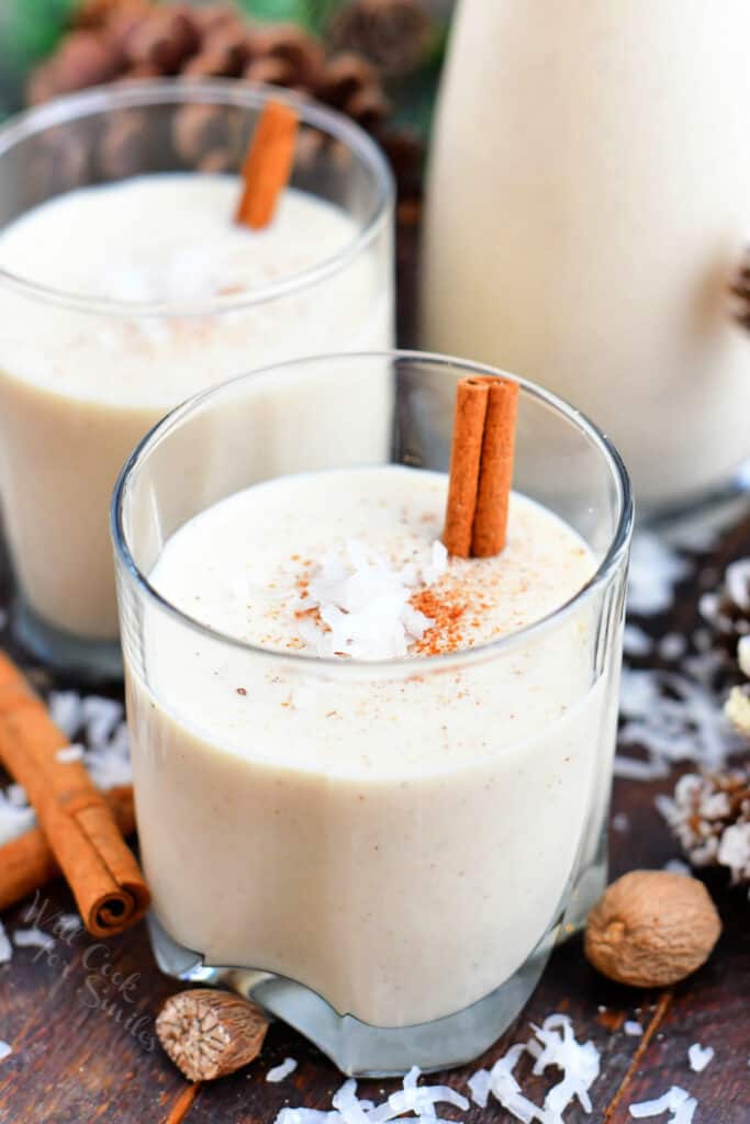 2 glasses of coquito garnished with cinnamon sticks and coconut flakes