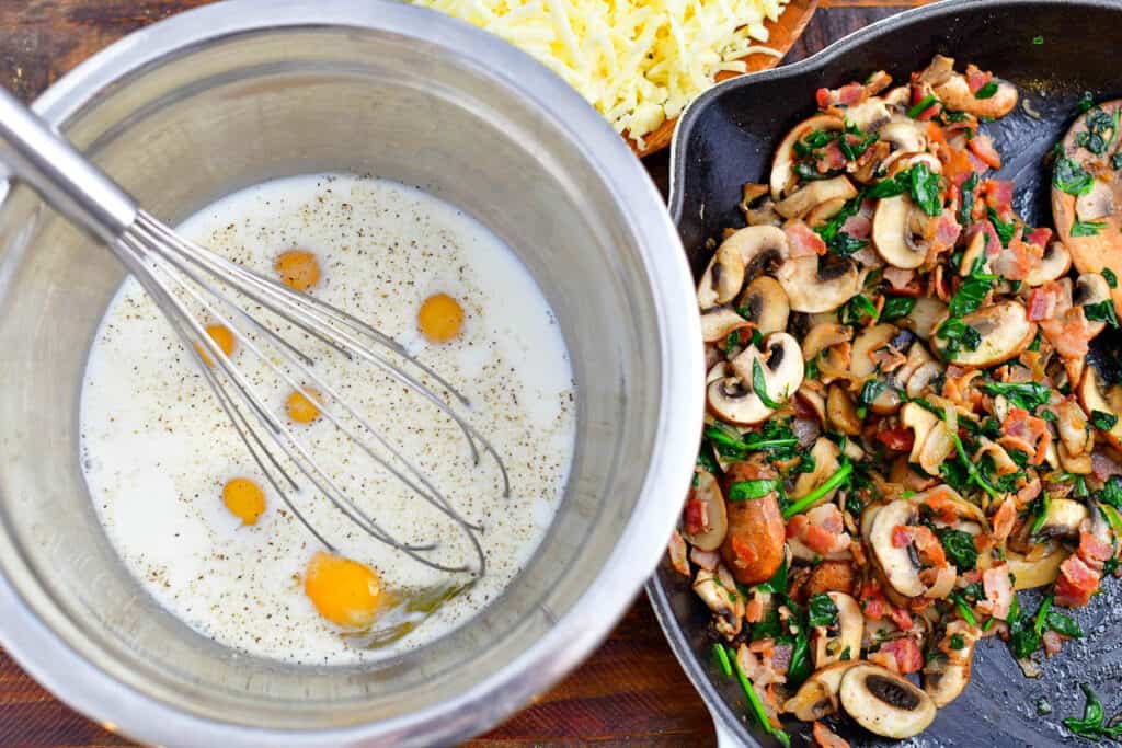 Eggs are whisked in a large metal bowl next to a serving of chopped vegetables.