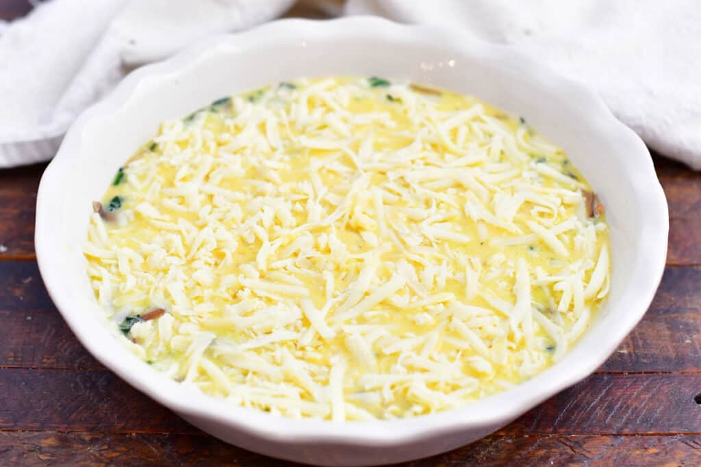 Grated cheese is spread on top of the uncooked egg mixture.