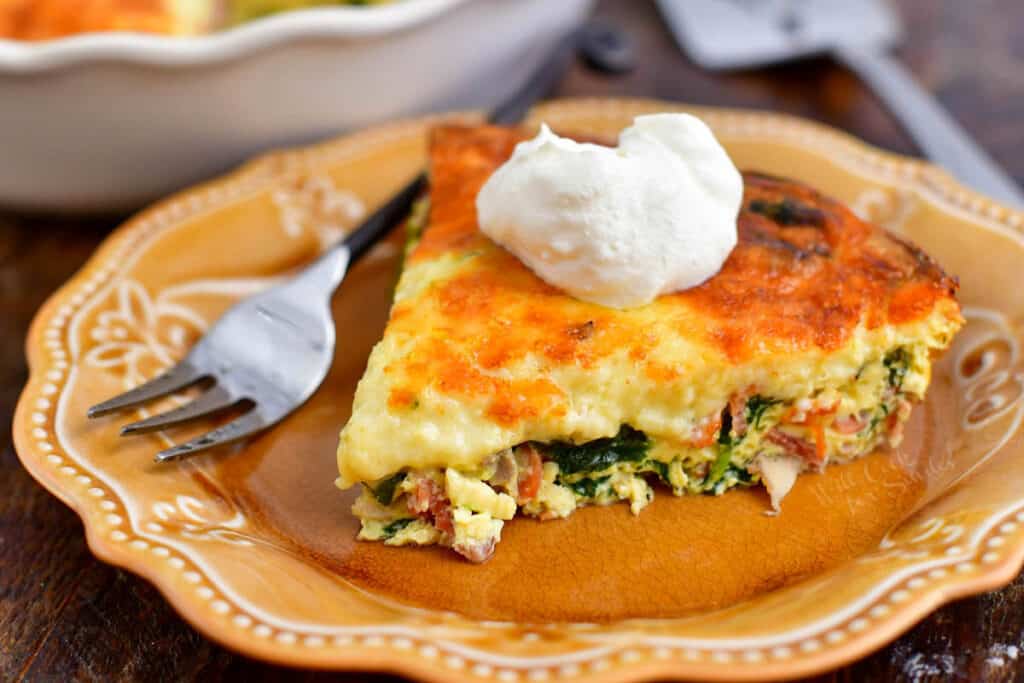 A slice of crustless quiche on a brown plate with a dollop of sour cream on top.