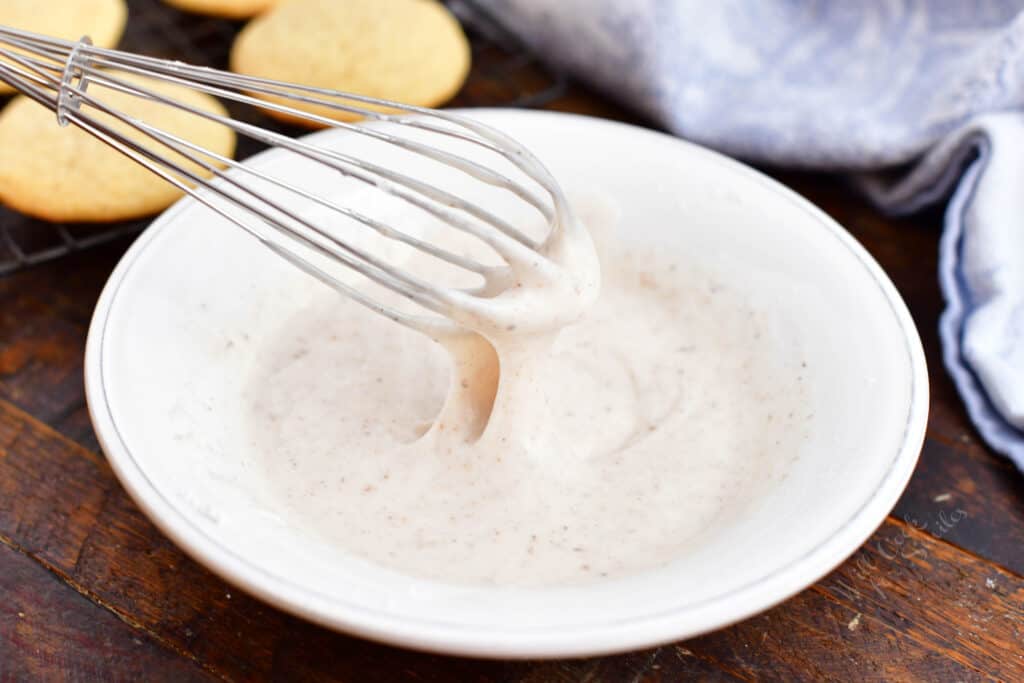 White icing is whisked in a shallow white bowl.
