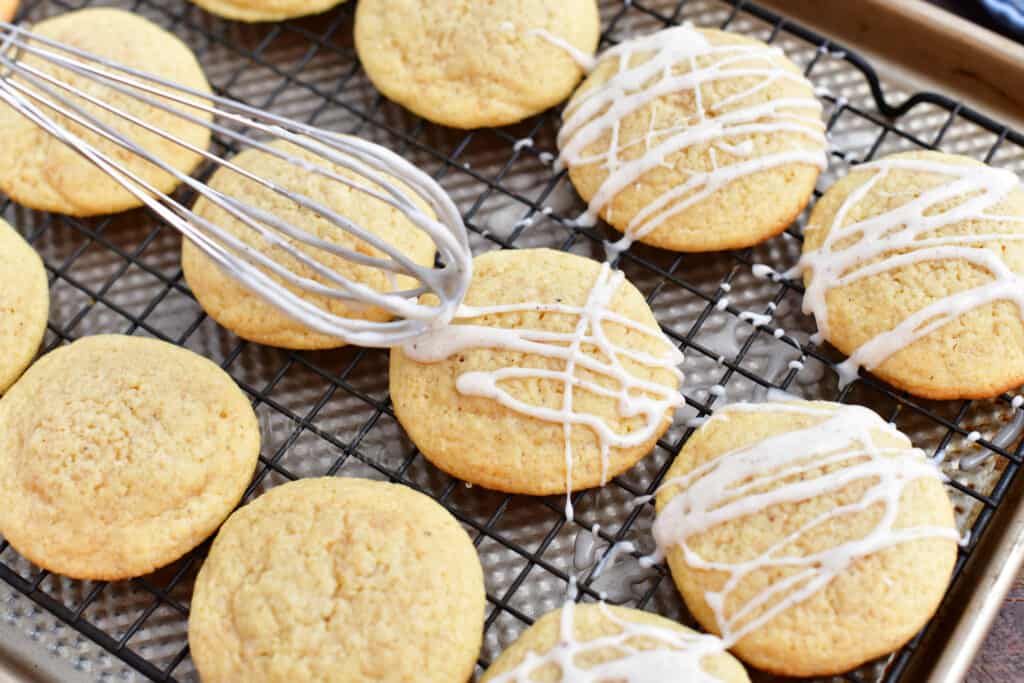 Icing is drizzled from a whisk onto the freshly baked cookies.