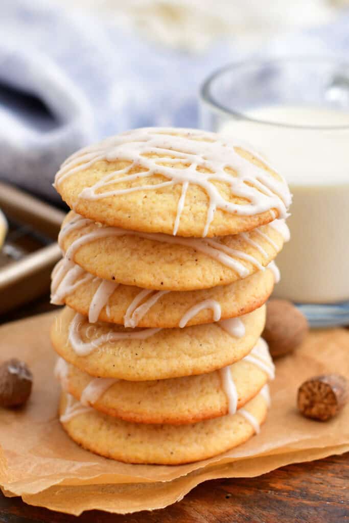 Eggnog cookies are stacked on an orange napkin, next to a glass of milk.