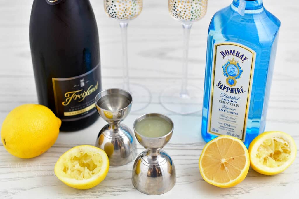 The ingredients and tools needed to make a French 75 recipe, on a white surface.